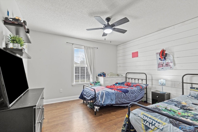 bedroom with ceiling fan, wooden walls, a textured ceiling, and hardwood / wood-style flooring