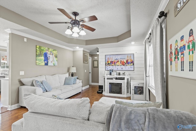 living room with a tray ceiling, crown molding, ceiling fan, and hardwood / wood-style flooring