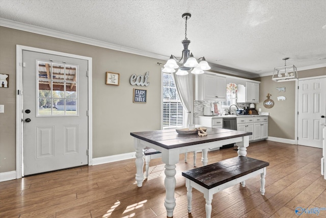 dining room with a textured ceiling, light wood-type flooring, an inviting chandelier, and crown molding