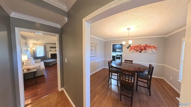 dining area with a textured ceiling, ornamental molding, a chandelier, and wood finished floors