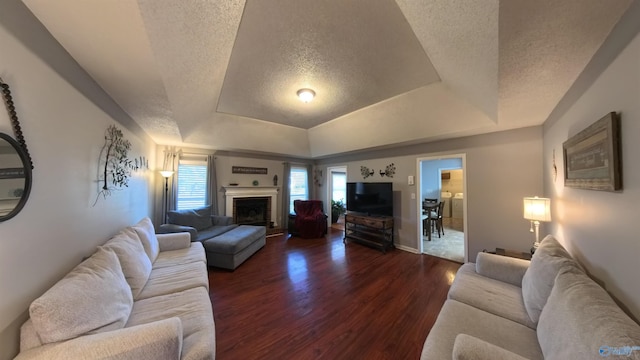 living room featuring a tray ceiling, a fireplace, dark wood finished floors, and a textured ceiling