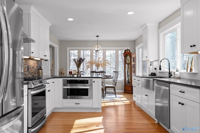 kitchen featuring appliances with stainless steel finishes, dark countertops, white cabinetry, and decorative light fixtures