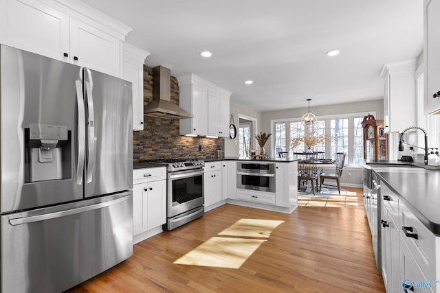 kitchen with decorative light fixtures, dark countertops, appliances with stainless steel finishes, white cabinets, and wall chimney range hood