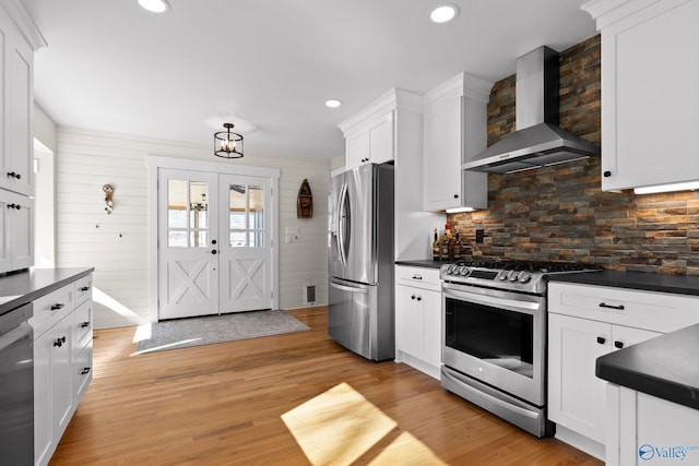 kitchen featuring light wood-style flooring, white cabinetry, wall chimney range hood, appliances with stainless steel finishes, and dark countertops