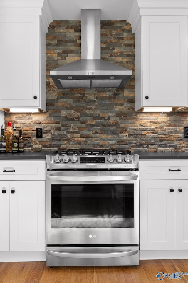 kitchen featuring dark countertops, white cabinets, wall chimney range hood, and gas range