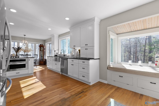 kitchen with white cabinets, appliances with stainless steel finishes, decorative light fixtures, light countertops, and light wood-style floors