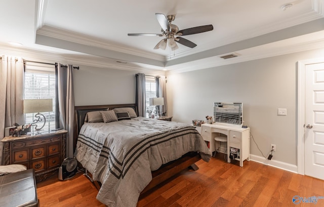 bedroom with hardwood / wood-style flooring, ceiling fan, multiple windows, and a tray ceiling