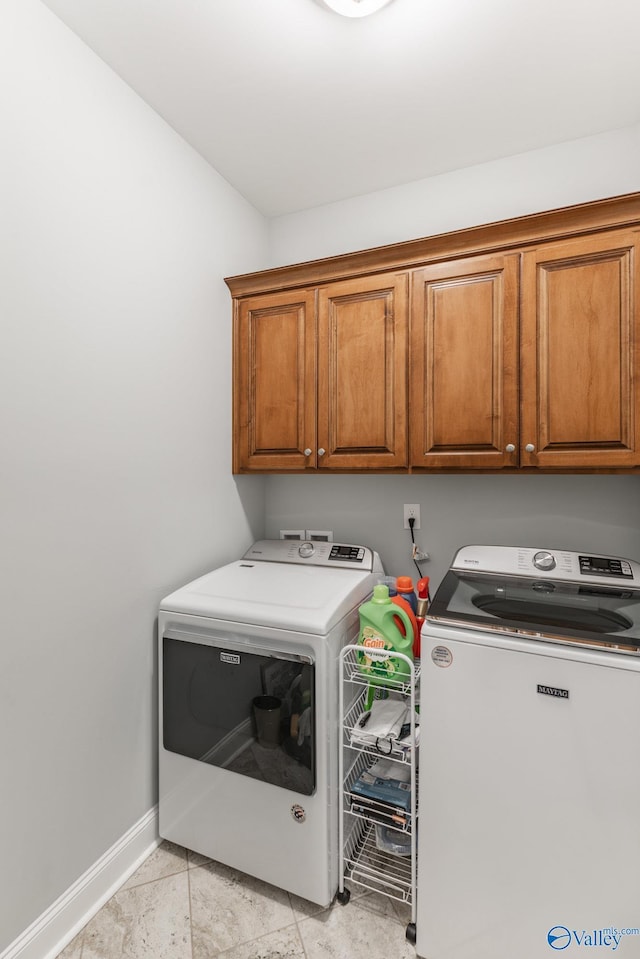 clothes washing area featuring cabinets, light tile patterned floors, and washing machine and clothes dryer