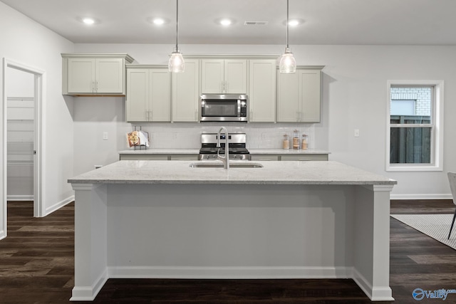 kitchen featuring an island with sink, appliances with stainless steel finishes, and light stone counters