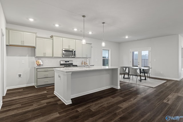 kitchen with stainless steel appliances, an island with sink, dark wood-type flooring, and decorative light fixtures