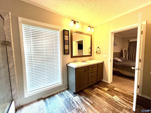 ensuite bathroom featuring a textured ceiling, a sink, wood finished floors, double vanity, and ensuite bath