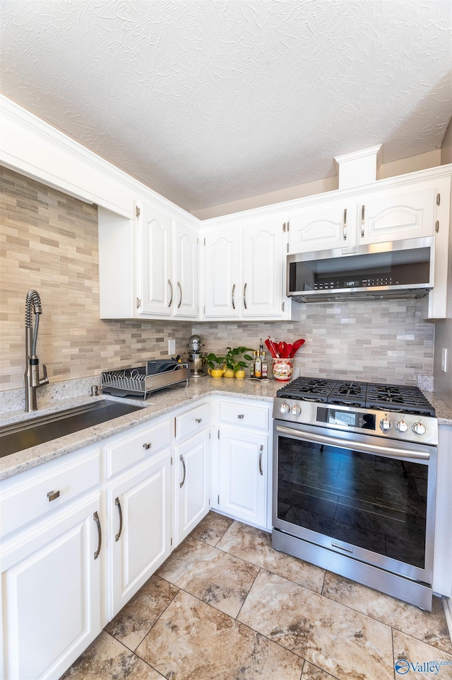 kitchen with gas range, white cabinetry, range hood, and backsplash