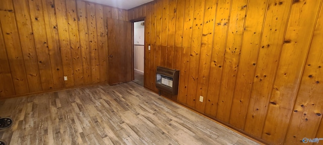 empty room featuring heating unit, light wood-type flooring, and wood walls