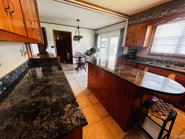 kitchen featuring a center island, crown molding, decorative light fixtures, light tile patterned floors, and a sink