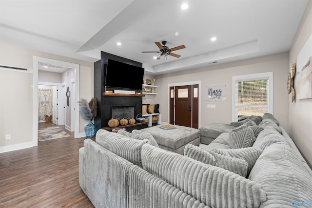 living room featuring a large fireplace, dark hardwood / wood-style floors, ceiling fan, and a tray ceiling