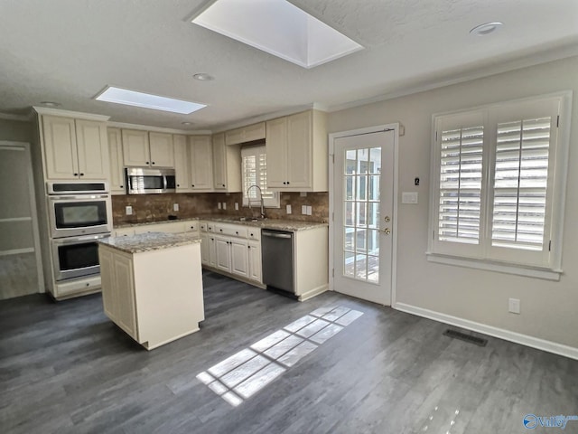 kitchen with dark wood-type flooring, sink, a skylight, appliances with stainless steel finishes, and a kitchen island