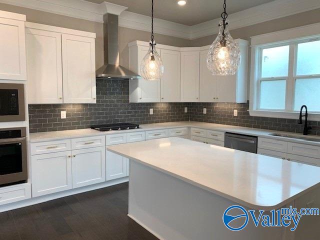 kitchen featuring sink, appliances with stainless steel finishes, wall chimney exhaust hood, tasteful backsplash, and pendant lighting