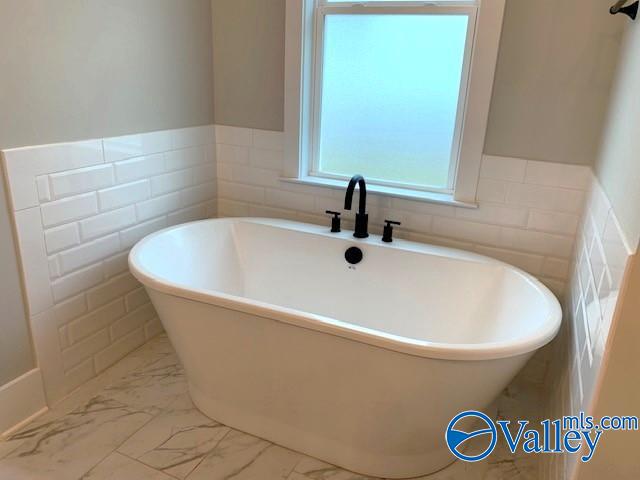 bathroom featuring tile walls, tile patterned flooring, and a tub to relax in