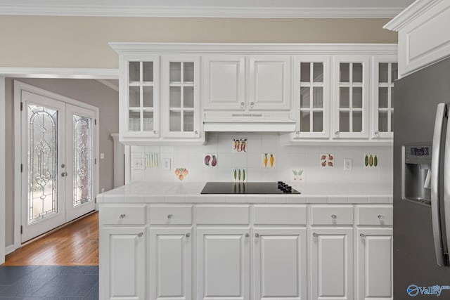 kitchen featuring tile countertops, white cabinets, stainless steel fridge, ornamental molding, and black electric stovetop