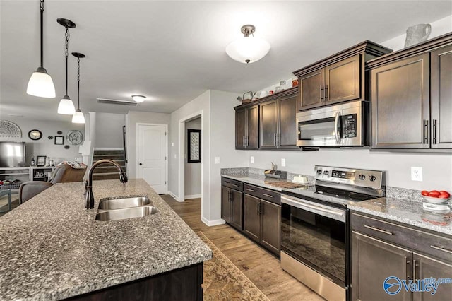 kitchen with a center island with sink, hanging light fixtures, appliances with stainless steel finishes, dark brown cabinetry, and a sink