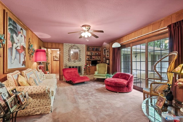 carpeted living room with a fireplace, a textured ceiling, wooden walls, and ceiling fan