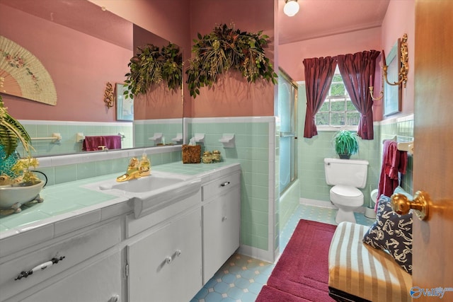 bathroom with combined bath / shower with glass door, a wainscoted wall, toilet, tile walls, and vanity