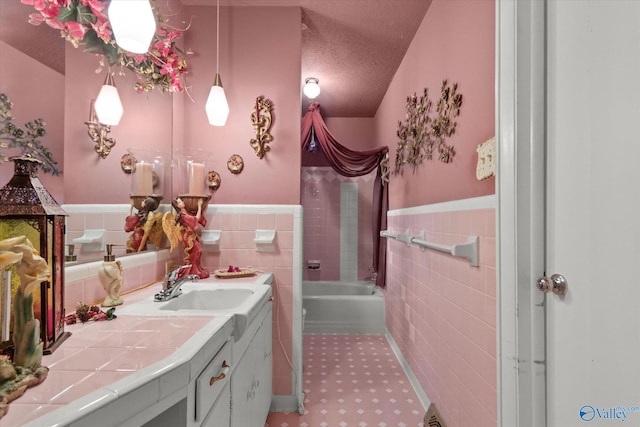 full bathroom with tile walls, a bathing tub, vanity, a textured ceiling, and wainscoting