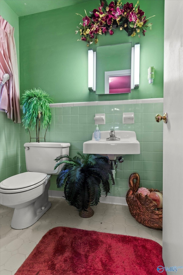 half bathroom with a sink, toilet, a wainscoted wall, and tile walls