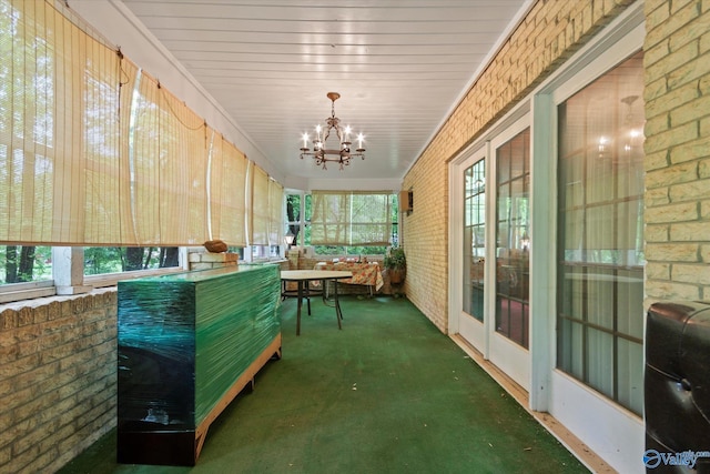 sunroom featuring a notable chandelier, carpet floors, and brick wall