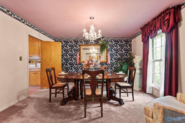 carpeted dining room featuring baseboards, wallpapered walls, an inviting chandelier, and an accent wall