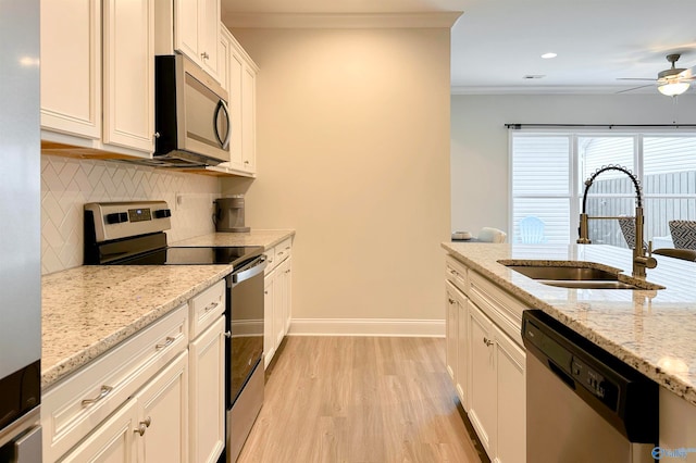 kitchen with stainless steel appliances, sink, light stone counters, backsplash, and light hardwood / wood-style flooring