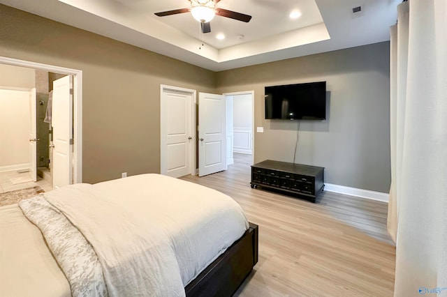 bedroom featuring ensuite bath, wood-type flooring, ceiling fan, and a tray ceiling