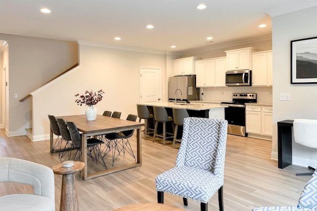 interior space with white cabinets, stainless steel appliances, a center island with sink, and light hardwood / wood-style flooring