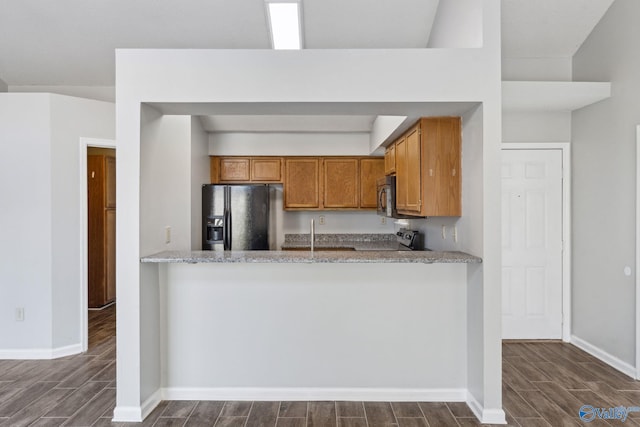 kitchen featuring light stone countertops, black fridge, and kitchen peninsula