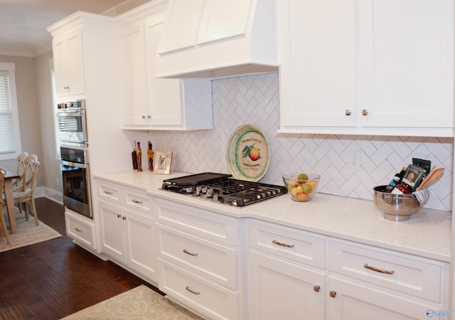 kitchen featuring dark wood-type flooring, premium range hood, white cabinetry, appliances with stainless steel finishes, and decorative backsplash