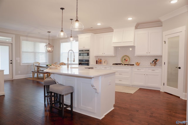 kitchen featuring an island with sink, dark hardwood / wood-style floors, pendant lighting, and white cabinets