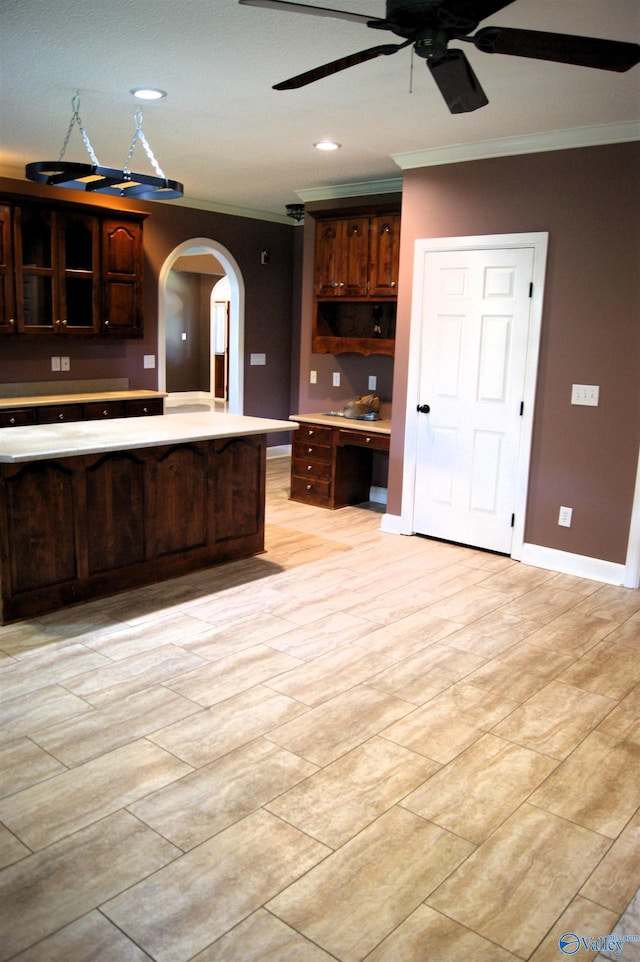 kitchen with ceiling fan, dark brown cabinetry, light countertops, ornamental molding, and arched walkways