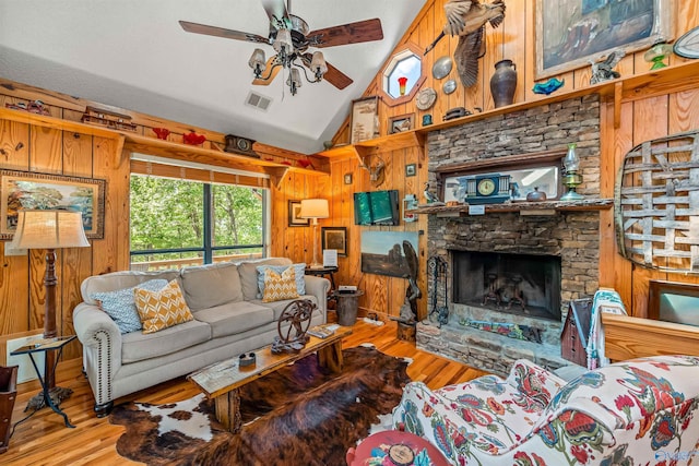 living room featuring ceiling fan, vaulted ceiling, light hardwood / wood-style flooring, and wood walls