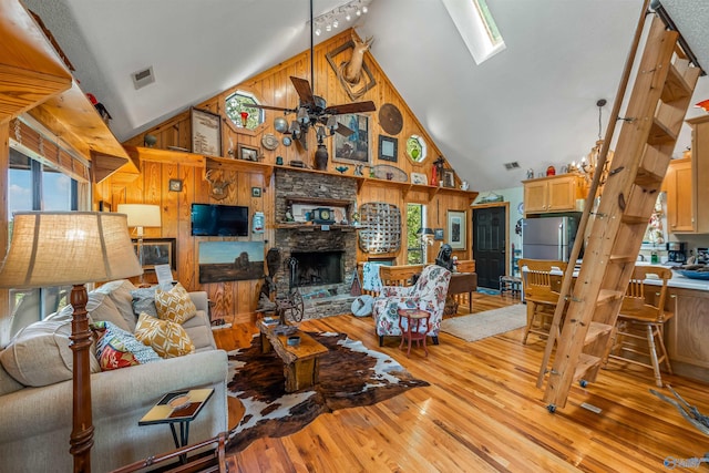 living room with a fireplace, light wood-type flooring, a skylight, high vaulted ceiling, and wood walls