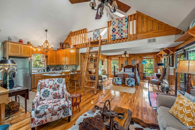 living room with sink, high vaulted ceiling, ceiling fan with notable chandelier, and light wood-type flooring