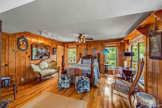 bedroom with a textured ceiling, light wood-type flooring, and wooden walls