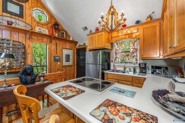 kitchen with wood walls, sink, lofted ceiling, and hanging light fixtures