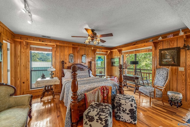 bedroom featuring multiple windows, wood walls, and light wood-type flooring