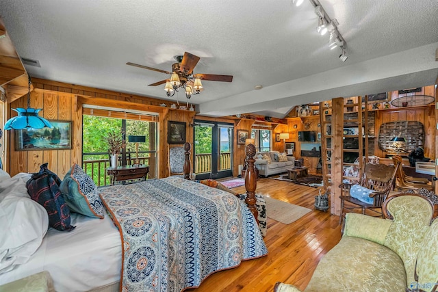 bedroom with light wood-type flooring, ceiling fan, a textured ceiling, and wooden walls