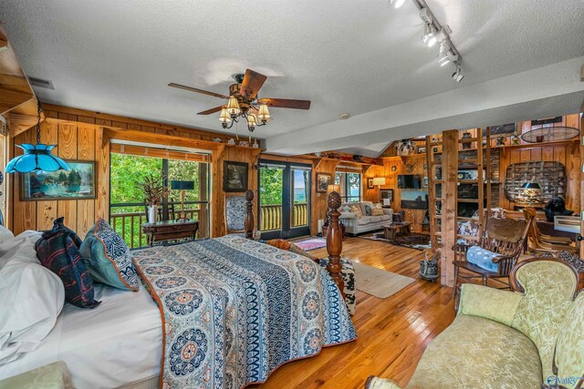 bedroom featuring wood walls, light hardwood / wood-style floors, a textured ceiling, and access to outside