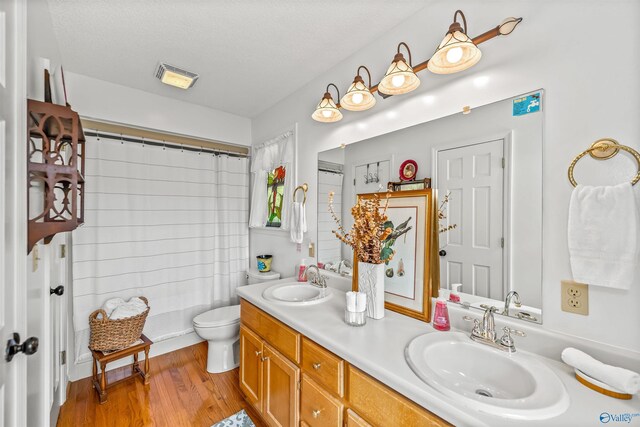 bathroom featuring hardwood / wood-style flooring, a textured ceiling, toilet, and dual bowl vanity