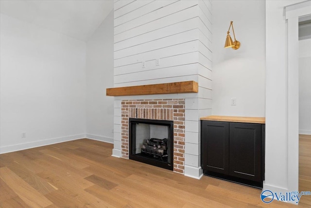 unfurnished living room with baseboards, a high ceiling, light wood-type flooring, and a brick fireplace