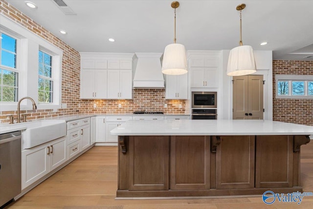 kitchen with brick wall, stainless steel appliances, white cabinets, custom exhaust hood, and a center island