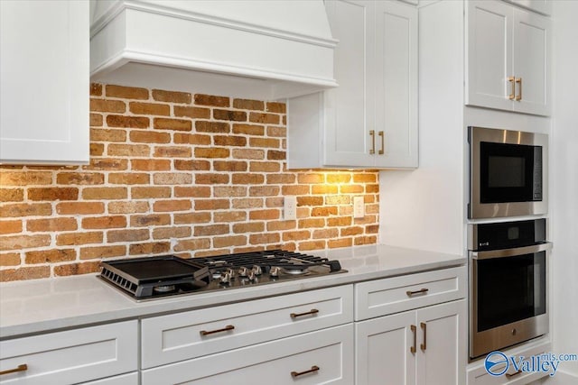 kitchen with stainless steel appliances, white cabinetry, and light stone counters