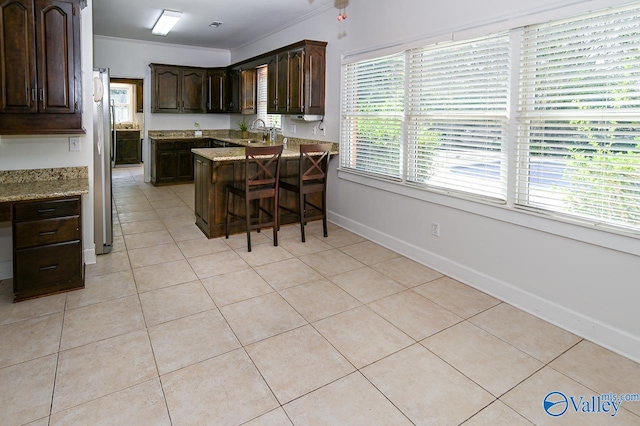 kitchen with light tile patterned flooring, crown molding, dark brown cabinets, and light stone counters